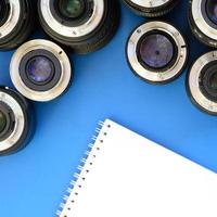 Several photographic lenses and white notebook lie on a bright blue background. Space for text photo