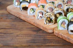 el juego de sushi de varios rollos se encuentra en una tabla de cortar de madera sobre una mesa en la cocina de un bar de sushi. un plato tradicional de la cocina oriental