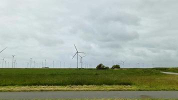 Blick aus einem fahrenden Auto auf große Windkraftanlagen in einem großen Windpark in Norddeutschland. video