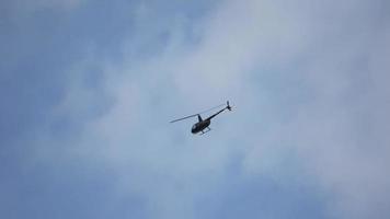 Ein kleiner dunkler Hubschrauber fliegt eine Kurve vor einem blauen und bewölkten Himmel. video
