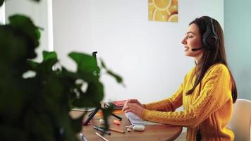 gelukkig vrouw in hoofdtelefoons is verloofd e aan het leren door web cam babbelen Bij huis. jong vrouw leerling in geel trui Aan laptop communiceren online door video telefoongesprek. afstand onderwijs en modern tech concept.