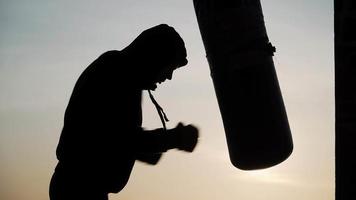 boxeur silhouette sur fond d'un magnifique coucher de soleil frappe un sac de boxe rapidement à l'échec. fatigue, ne peut plus faire d'exercice. motivation. sports et arts martiaux. video