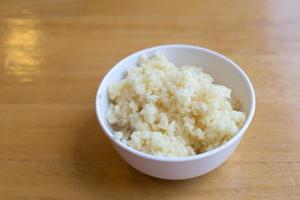 Chopped garlic is put in a white cup on the wooden table. photo