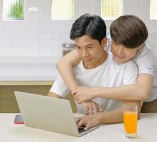 Young LGBT couple domestic life concept. Asian young LGBT male hugging his boyfriend while working with laptop computer at home in the morning with happy smiling face. Selective focus. photo