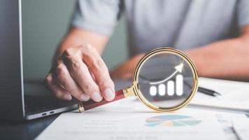 Businessman holding a magnifying glass showing business growth concept, developing potential with marketing strategy, trending graph showing increasing profits. about finance and investment photo