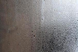 textura de una gota de lluvia sobre un fondo transparente húmedo de vidrio. tonificado en color gris