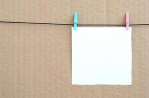 White blank card on rope on a brown cardboard background. Creative reminder, small sheet of paper on wooden clothespin, memo backdrop photo