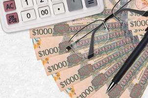 Ventilador de billetes de 1000 dólares guyaneses y calculadora con gafas y bolígrafo. préstamo comercial o concepto de temporada de pago de impuestos foto