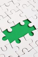 Close-up texture of a white jigsaw puzzle in assembled state with missing elements forming a green pad for text. Copy space photo