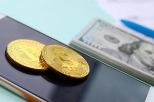 bitcoins se encuentra con los formularios de impuestos, los billetes de cien dólares y el teléfono inteligente en un fondo azul claro. declaración de la renta foto