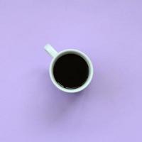 pequeña taza de café blanca sobre fondo de textura de papel de color violeta pastel de moda en concepto mínimo foto