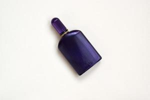 Dark purple perfume bottle with golden ribbon on pastel paper background. Trendy fragrance photo