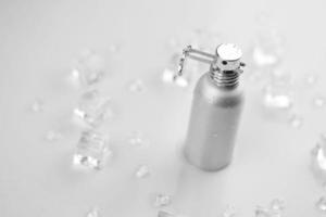 frasco plateado de perfume femenino, fotografía objetiva de frasco de perfume metálico en cubitos de hielo y agua sobre mesa blanca. vista desde arriba. foto de producto de maqueta, concepto de frescura