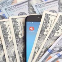 KHARKOV, UKRAINE - JULY 2, 2021 Smartphone screen with Pinterest app and lot of hundred dollar bills. Business and social networking concept photo
