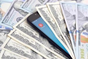 KHARKOV, UKRAINE - JULY 2, 2021 Smartphone screen with Pinterest app and lot of hundred dollar bills. Business and social networking concept photo