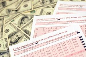 Pink gambling sheets with numbers for marking on big amount of hundred dollar bills. Lottery playing concept or gambling addiction. Close up photo