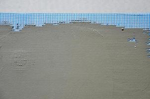 The texture of the wall, covered with gray foam polystyrene plates, covered with a blue reinforcing mesh and covered with a mixture for gluing it. Stage of wall insulation photo