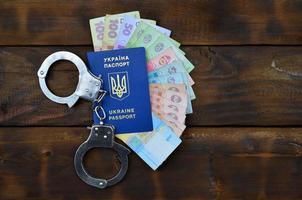 A photograph of a Ukrainian foreign passport, a certain amount of Ukrainian money and police handcuffs. Concept of illegal earnings of Ukrainian citizens abroad photo