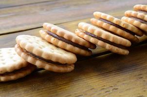 A round sandwich cookie with coconut filling lies in large quantities on a brown wooden surface. Photo of edible treats on a wooden background with copy space