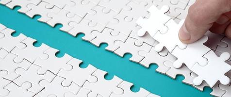 The human hand paves the way to the surface of the jigsaw puzzle, forming a blue space. The concept of overcoming the difficulties on the way to success photo