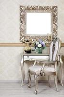 A fragment of a retro interior with a chair and table, on which is a telephone and a vase of flowers. Above the table hangs an empty picture frame for your photo