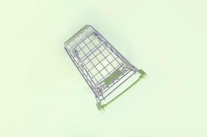 Small shopping cart lies on a lime background. Minimalism flat lay photo