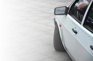 Diagonal view of a white glossy car that stands on a square of gray tiles photo