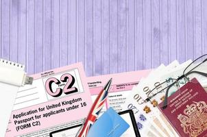 English form C2 Application for United Kingdom passport for applicants under 16 lies on table with office items. UK passport paperwork photo