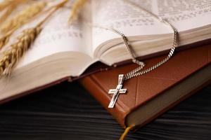 Silver necklace with crucifix cross on christian holy bible book on black wooden table. Asking blessings from God with the power of holiness photo