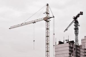 grúas altas de trabajo dentro del lugar con edificios altos en construcción contra un cielo azul claro. Grúa y construcción de progreso de trabajo. tono retro foto