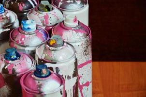 Still life with a large number of used colorful spray cans of aerosol paint lying on the treated wooden surface in the artist's graffiti workshop. Dirty and stained cans for spray art photo