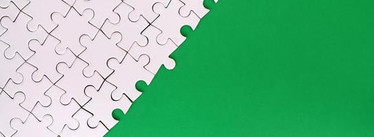 Fragment of a folded white jigsaw puzzle on the background of a green plastic surface. Texture photo with copy space for text