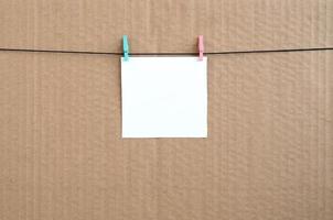 White blank card on rope on a brown cardboard background. Creative reminder, small sheet of paper on wooden clothespin, memo backdrop photo