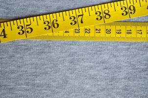 Yellow measuring tape lies on a gray knitted fabric photo