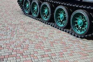 A military vehicle on caterpillar tracks stands on a square of paving stones. Photo of green caterpillars with metal wheels that rotate them