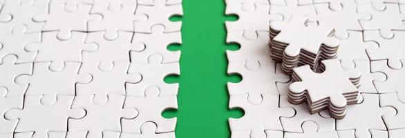 The green path is laid on the platform of a white folded jigsaw puzzle. The missing elements of the puzzle are stacked nearby. Texture image with space for text photo