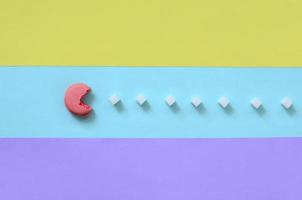 A composition of macaroon with an open mouth that is going to eat sugar cubes on a blue, pink, yellow and violet pastel background. The concept of old video games photo