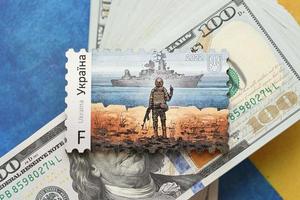 TERNOPIL, UKRAINE - SEPTEMBER 2, 2022 Famous Ukrainian postmark with russian warship and ukrainian soldier as wooden souvenir on big amount of US dollar bills photo