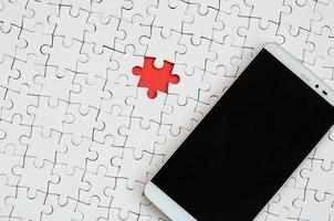 A modern big smartphone with a touch screen lies on a white puzzle puzzle in an assembled state photo