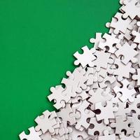 A pile of uncombed elements of a white jigsaw puzzle lies on the background of a green surface. Texture photo with copy space for text