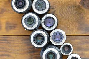 Several photographic lenses lie on a brown wooden background. Space for text photo