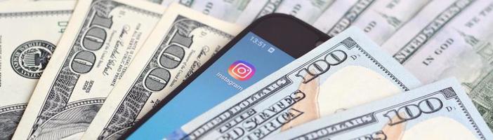 KHARKIV, UKRAINE - MAY 4, 2020 Smartphone screen with Instagram app and lot of hundred dollar bills. Business and social networking concept photo