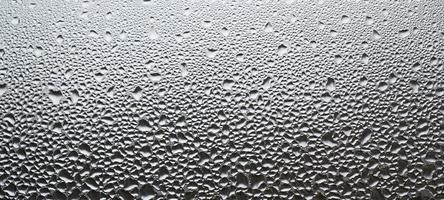 A photo of the glass surface of the window, covered with a multitude of droplets of various sizes. Background texture of a dense layer of condensate on glass