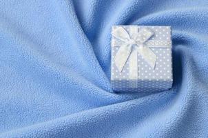 A small gift box in blue with a small bow lies on a blanket of soft and furry light blue fleece fabric with a lot of relief folds. Packing for a gift to your lovely girlfriend photo