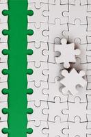 The green path is laid on the platform of a white folded jigsaw puzzle. The missing elements of the puzzle are stacked nearby. Texture image with space for text photo