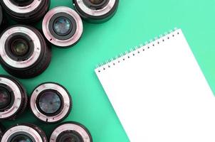 Several photographic lenses and white notebook lie on a bright turquoise background. Copy space photo