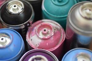 Large number of used colorful spray cans of aerosol paint lying on the treated wooden surface in the artist's graffiti workshop close up. Dirty and stained cans for art photo