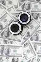 Two photographic lenses lie on the background of a lot of dollar bills. Space for text photo