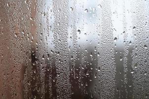 A photo of the glass surface of the window, covered with a multitude of droplets of various sizes. Background texture of a dense layer of condensate on glass