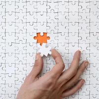 The texture of a white jigsaw puzzle in the assembled state with one missing element that the male hand puts in photo